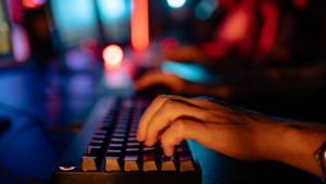 Hands typing on a keyboard in front of illuminated computer screens, representing virtual workplace communication and online workplace misconduct.